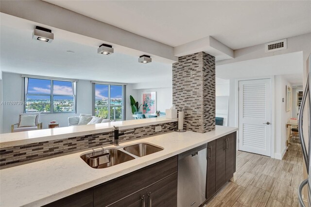 kitchen with stainless steel dishwasher, backsplash, a sink, visible vents, and dark brown cabinets