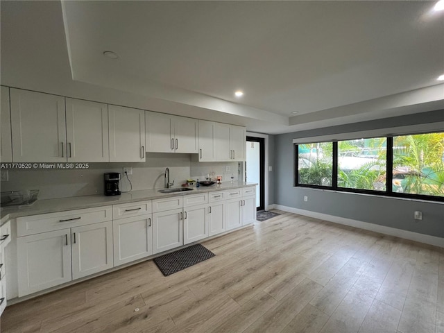 kitchen featuring a tray ceiling, a sink, light wood-type flooring, baseboards, and white cabinetry