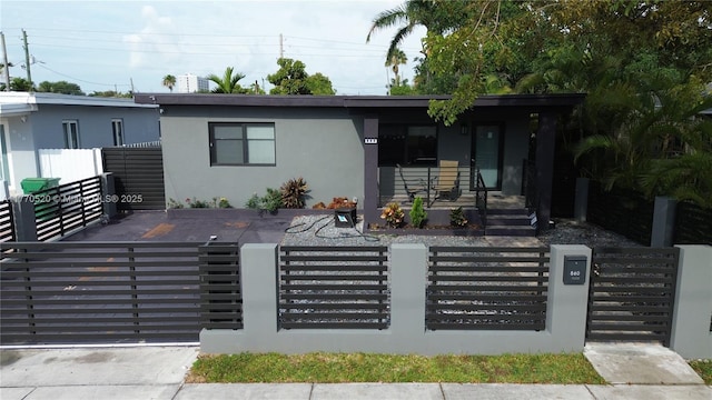 view of front facade featuring stucco siding, covered porch, a fenced front yard, and a gate