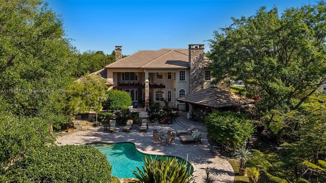 12483 Grand Oaks Dr, Davie, FL 33330 - back of property with a patio, a chimney, an outdoor pool, a tile roof, and stucco siding