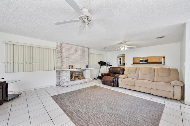 living room featuring a textured ceiling, visible vents, a brick fireplace, a ceiling fan, and light tile patterned floors