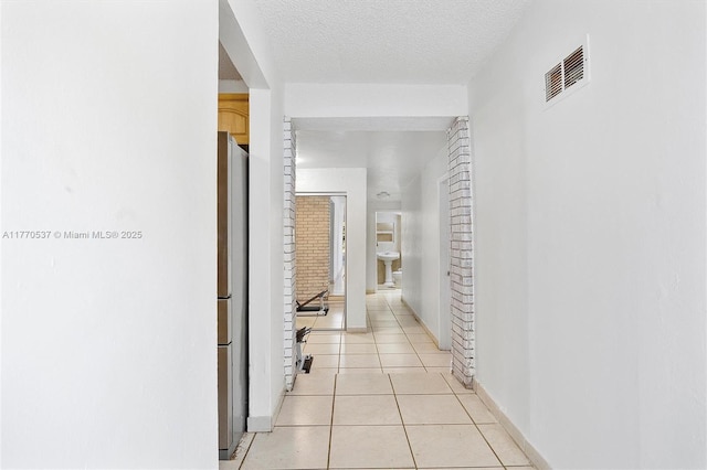 hall featuring light tile patterned flooring, baseboards, a textured ceiling, and visible vents