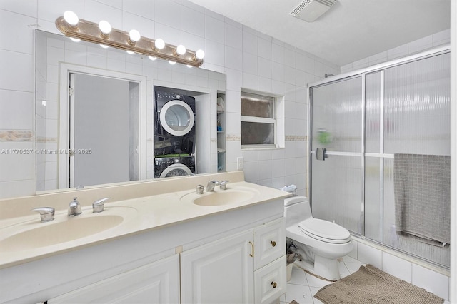 bathroom with stacked washer and clothes dryer, tile walls, a sink, a stall shower, and visible vents
