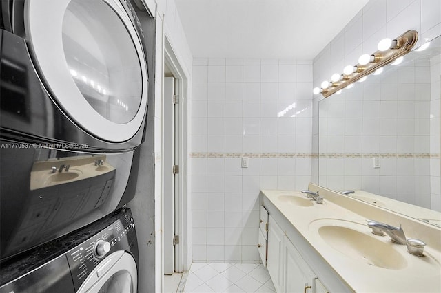 full bath with tile patterned floors, a sink, stacked washing maching and dryer, and tile walls