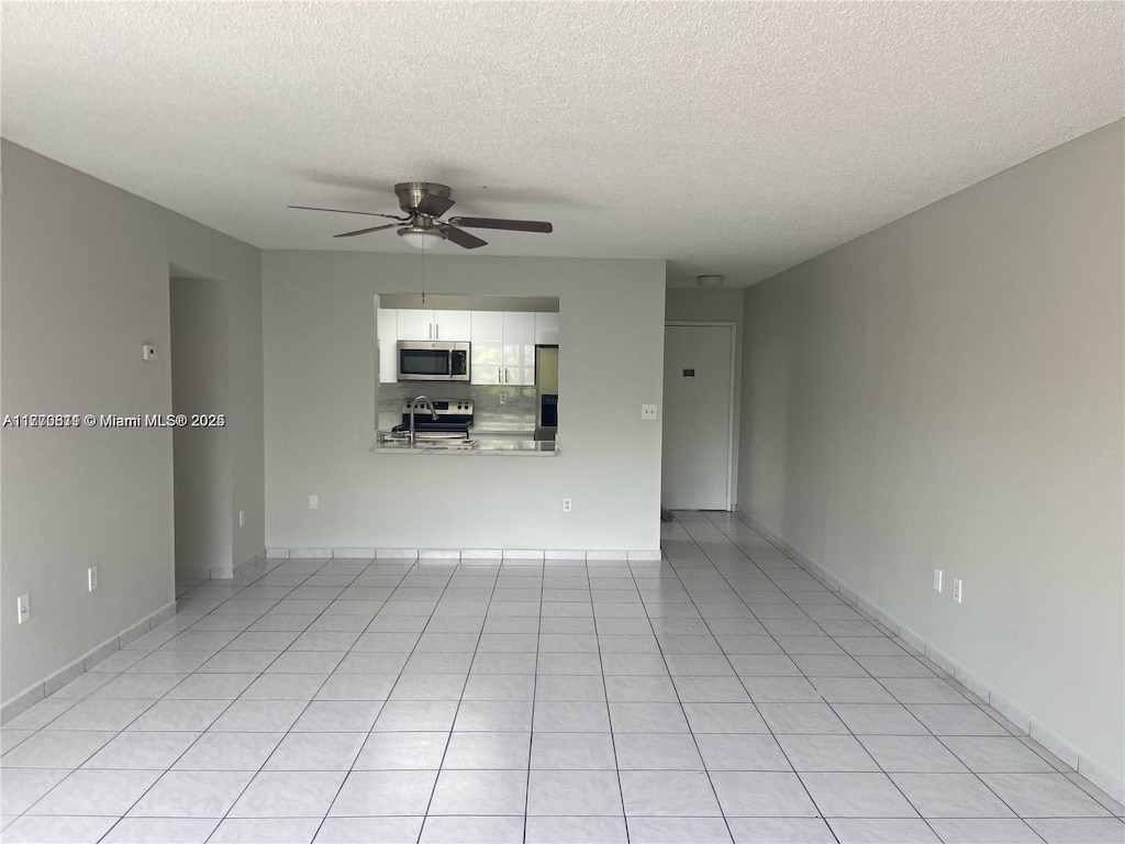 unfurnished living room with a textured ceiling, baseboards, light tile patterned floors, and a ceiling fan