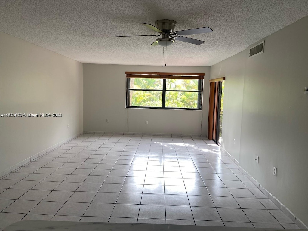 empty room featuring a textured ceiling, ceiling fan, visible vents, and light tile patterned floors