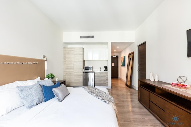 bedroom featuring baseboards, visible vents, freestanding refrigerator, and light wood finished floors