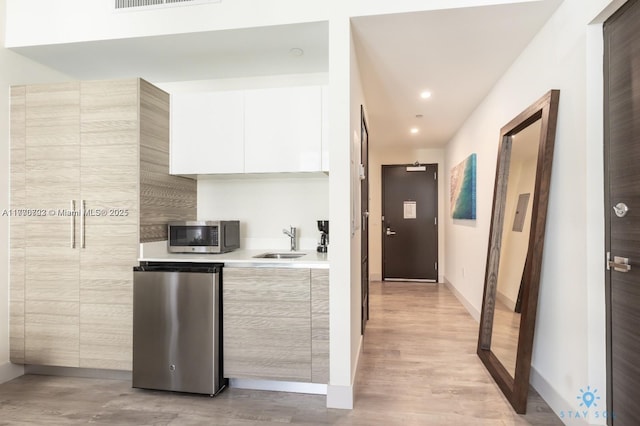 kitchen featuring light countertops, modern cabinets, stainless steel microwave, a sink, and fridge