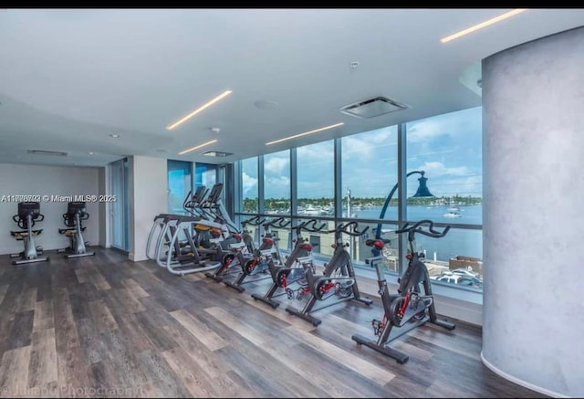 exercise room featuring floor to ceiling windows, visible vents, wood finished floors, and a water view