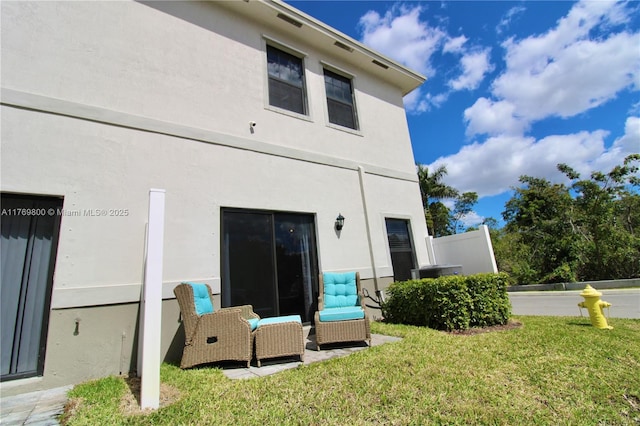 back of property featuring a lawn and stucco siding