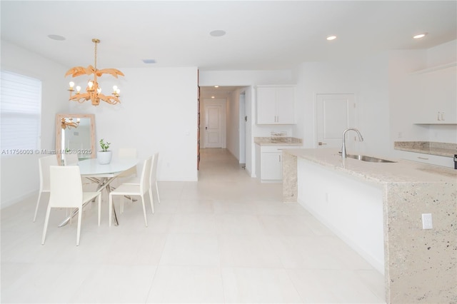 kitchen featuring a chandelier, recessed lighting, white cabinetry, a sink, and light stone counters