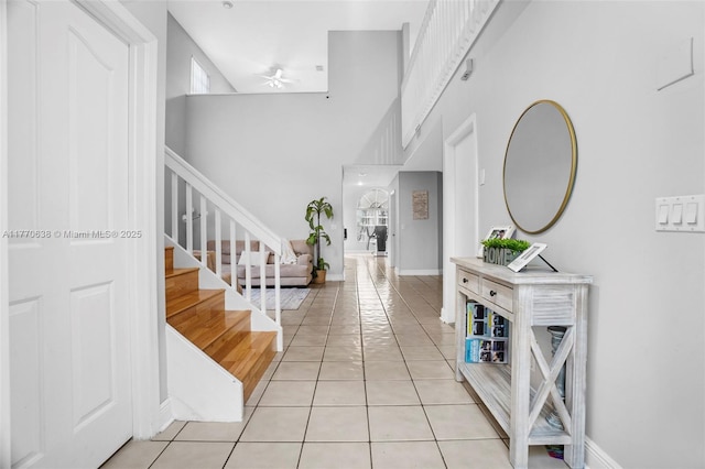 foyer entrance featuring ceiling fan, stairs, baseboards, light tile patterned floors, and a towering ceiling