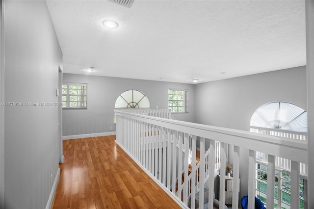 corridor featuring baseboards, a textured ceiling, wood finished floors, and visible vents