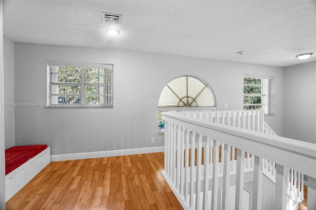 corridor with a textured ceiling, visible vents, wood finished floors, baseboards, and an upstairs landing