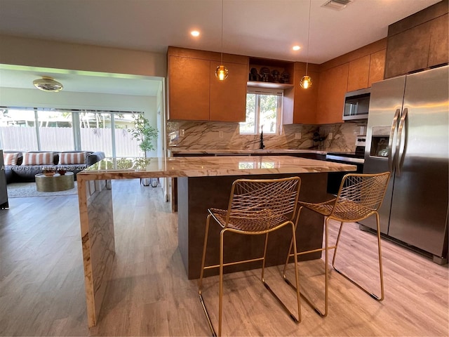 kitchen featuring light wood-style floors, a sink, backsplash, and appliances with stainless steel finishes
