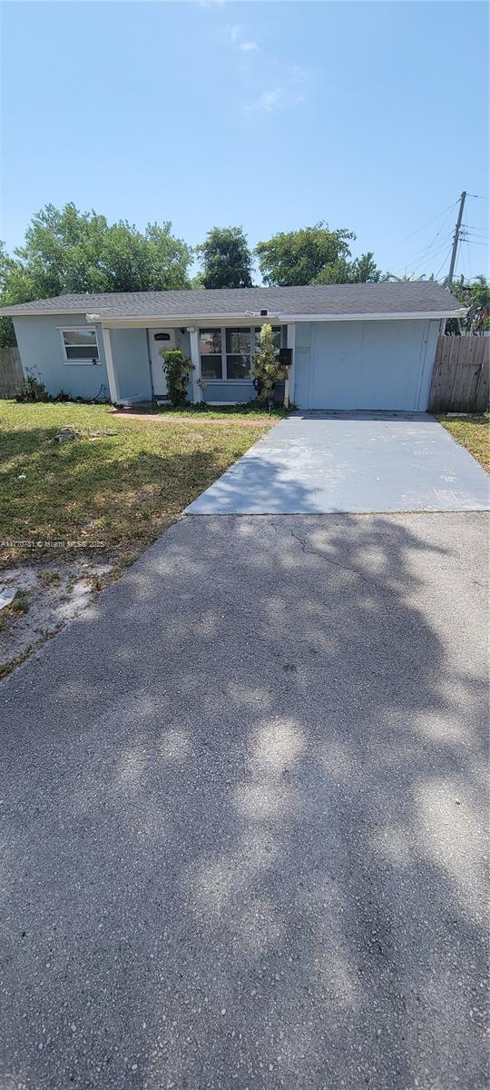 ranch-style home with concrete driveway, stucco siding, fence, and a front lawn
