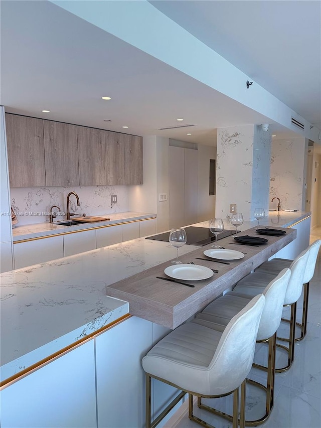 19707 Turnberry Way Unit 6E, Aventura, FL 33180 - kitchen featuring black electric cooktop, modern cabinets, a kitchen bar, a sink, and backsplash