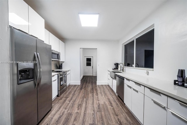 kitchen featuring light countertops, stainless steel appliances, dark wood-type flooring, white cabinetry, and a sink