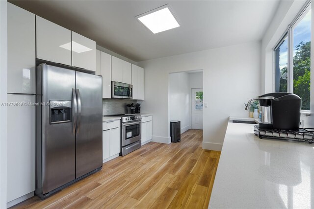 1114 SW 11th Ave, Miami, FL 33129 - kitchen featuring appliances with stainless steel finishes, white cabinetry, light wood-style floors, tasteful backsplash, and light countertops