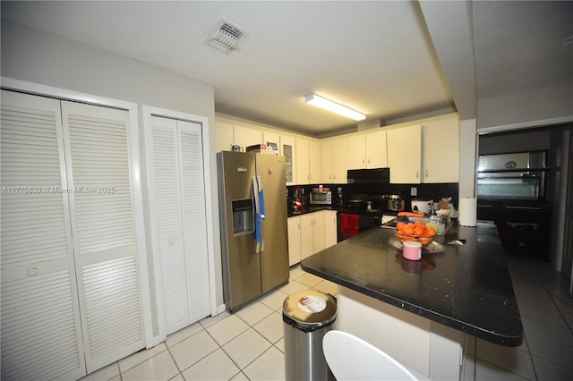 kitchen with visible vents, stainless steel fridge, a peninsula, dark countertops, and light tile patterned floors