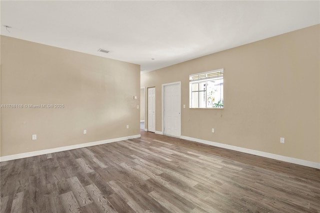 spare room with baseboards, visible vents, and wood finished floors
