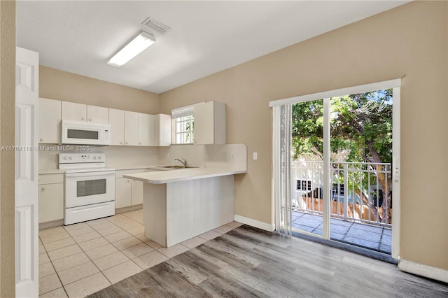 kitchen with light countertops, tasteful backsplash, a peninsula, white appliances, and visible vents