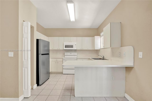 kitchen featuring light countertops, a sink, a peninsula, light tile patterned floors, and white appliances