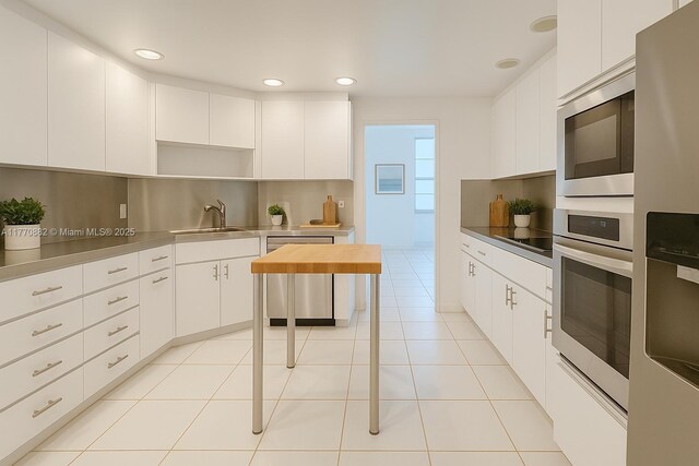 5255 Collins Ave Unit 5D, Miami Beach, FL 33140 - kitchen with stainless steel appliances, stainless steel counters, white cabinetry, recessed lighting, and light tile patterned floors