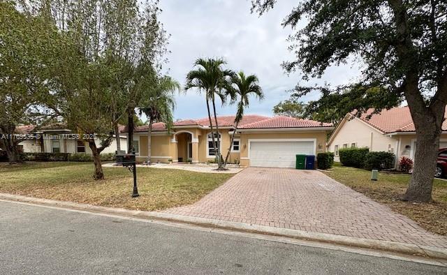 single story home with a tiled roof, decorative driveway, an attached garage, a front yard, and stucco siding