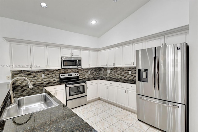 kitchen featuring lofted ceiling, white cabinetry, a sink, appliances with stainless steel finishes, and backsplash