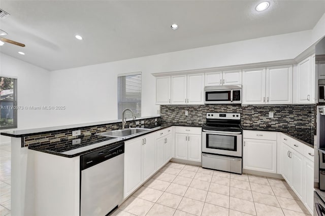 kitchen with dark countertops, appliances with stainless steel finishes, a sink, a peninsula, and decorative backsplash