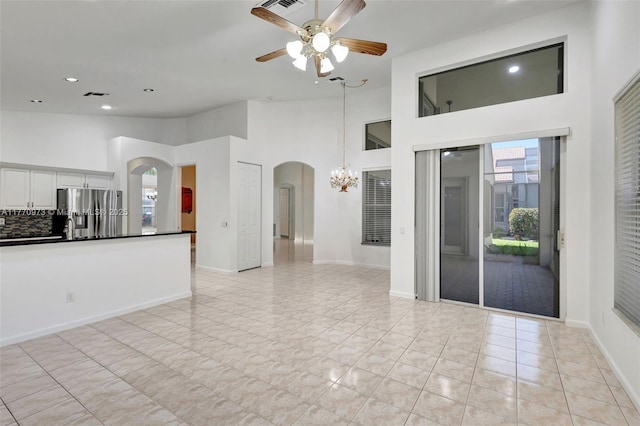 unfurnished living room with arched walkways, ceiling fan with notable chandelier, recessed lighting, a towering ceiling, and visible vents