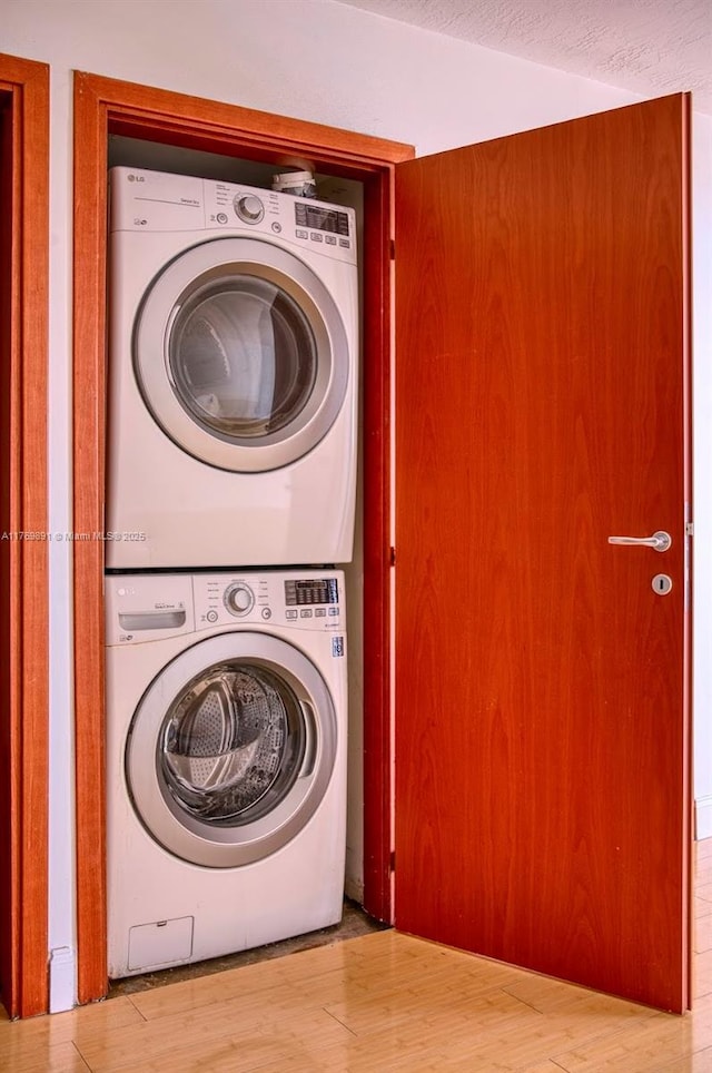 clothes washing area featuring wood finished floors, laundry area, and stacked washer / drying machine