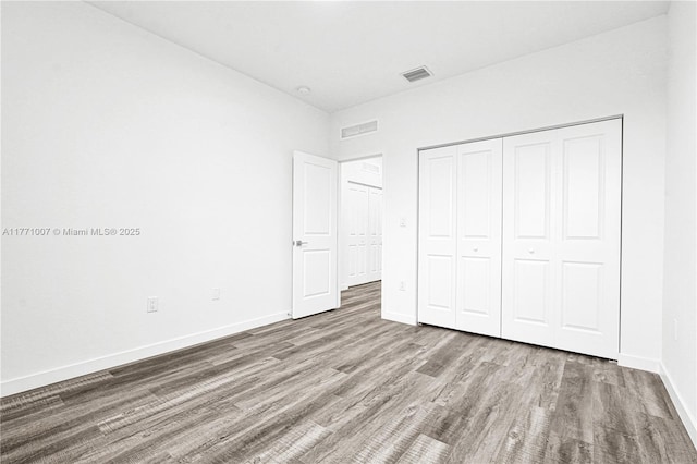 unfurnished bedroom with baseboards, visible vents, a closet, and wood finished floors