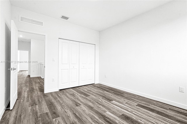 unfurnished bedroom with dark wood-style floors, visible vents, a closet, and baseboards