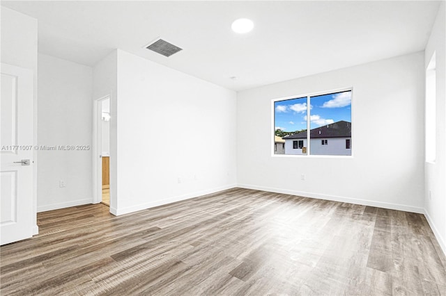empty room featuring baseboards, visible vents, and wood finished floors