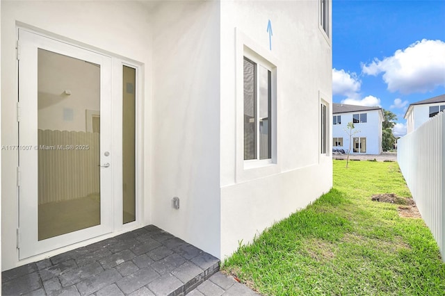 entrance to property with stucco siding, fence, a yard, and a patio area