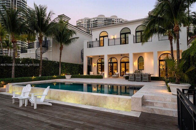 3918 Island Estates Dr, Aventura, FL 33160 - back of property at dusk featuring an outdoor pool, a patio area, stucco siding, and a balcony