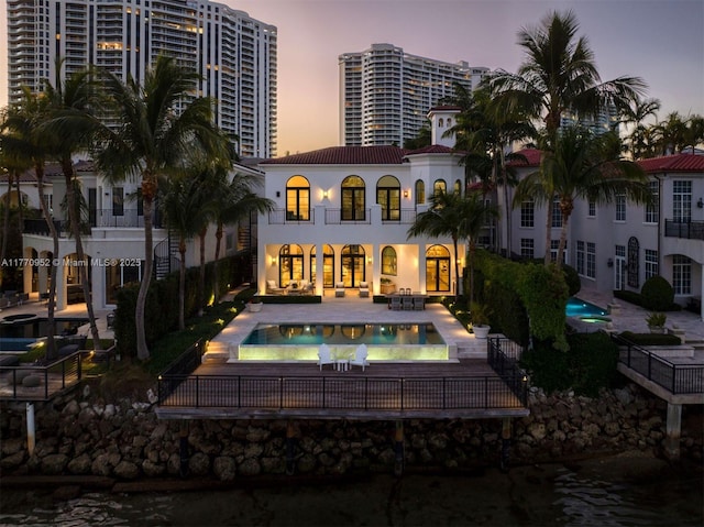 3918 Island Estates Dr, Aventura, FL 33160 - back of property at dusk featuring an outdoor pool, a tiled roof, a patio area, and stucco siding