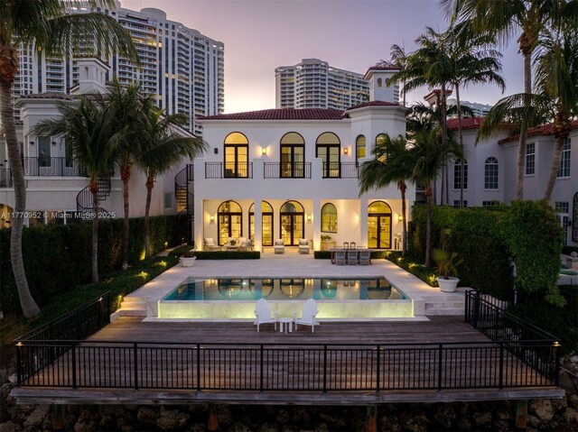 3918 Island Estates Dr, Aventura, FL 33160 - back of property at dusk featuring a tiled roof, a patio, a balcony, stucco siding, and a fenced in pool