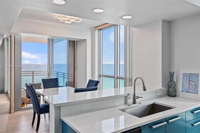 kitchen featuring light countertops, a sink, blue cabinets, and a water view