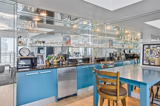 bar with a sink, black microwave, fridge, indoor wet bar, and light wood-style floors