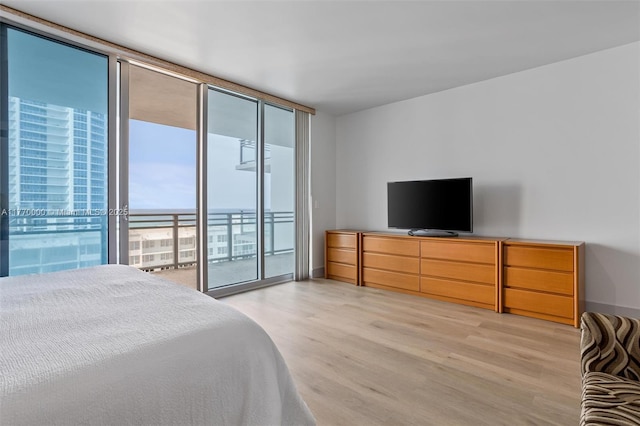 bedroom featuring light wood-style floors, access to outside, and a wall of windows