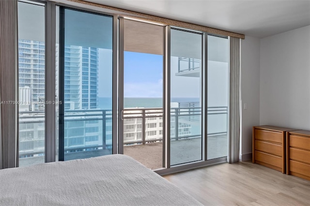 unfurnished bedroom featuring a water view, light wood finished floors, and a wall of windows