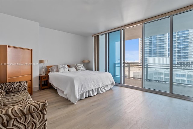 bedroom with expansive windows, access to exterior, and light wood-style floors
