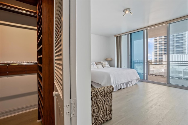 bedroom with a city view, expansive windows, wood finished floors, and access to outside