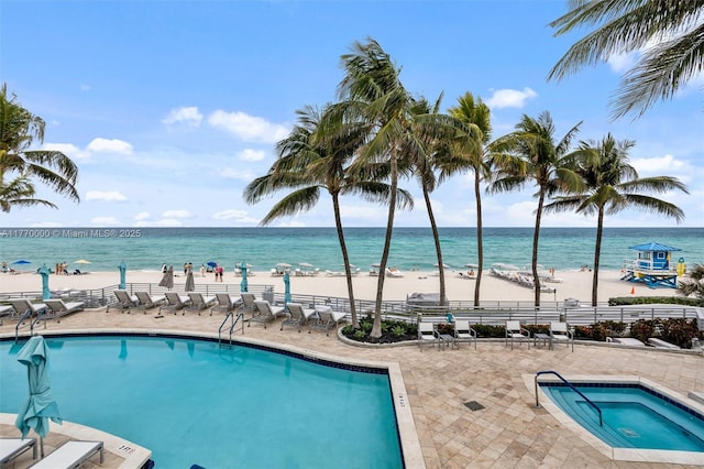 community pool featuring a community hot tub, a view of the beach, a water view, and a patio