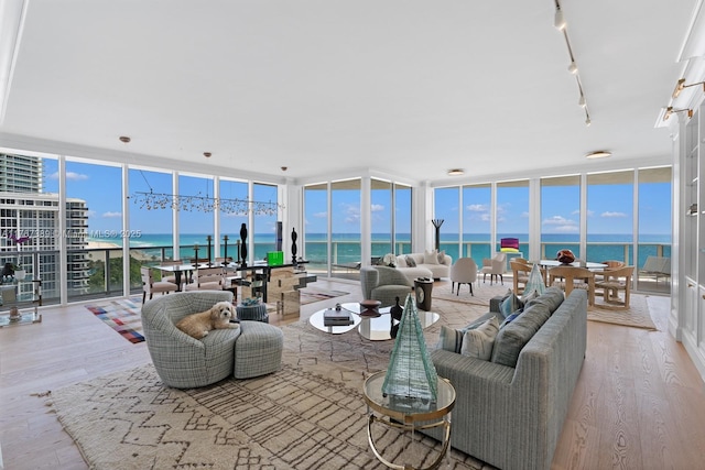 living room with a wall of windows, a water view, rail lighting, and wood finished floors
