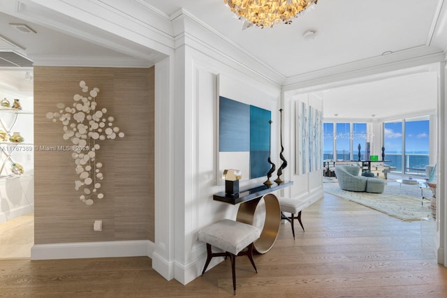 hallway featuring baseboards, ornamental molding, wood finished floors, and a chandelier
