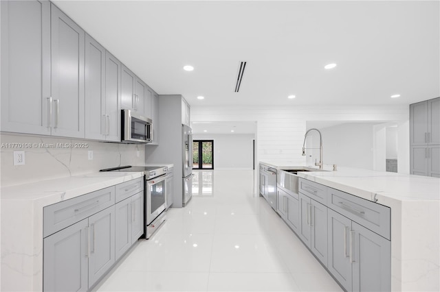 kitchen with stainless steel appliances, tasteful backsplash, a sink, light stone counters, and gray cabinets
